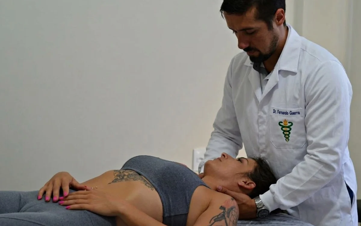 Dr. Fernando Guerra posiciona as mãos no pescoço e na base do crânio de uma paciente deitada